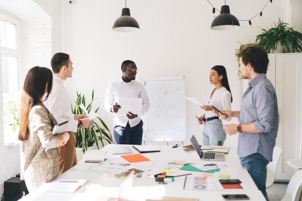 A diverse group of professionals gathered around a conference table in a modern office setting, engaged in discussion.