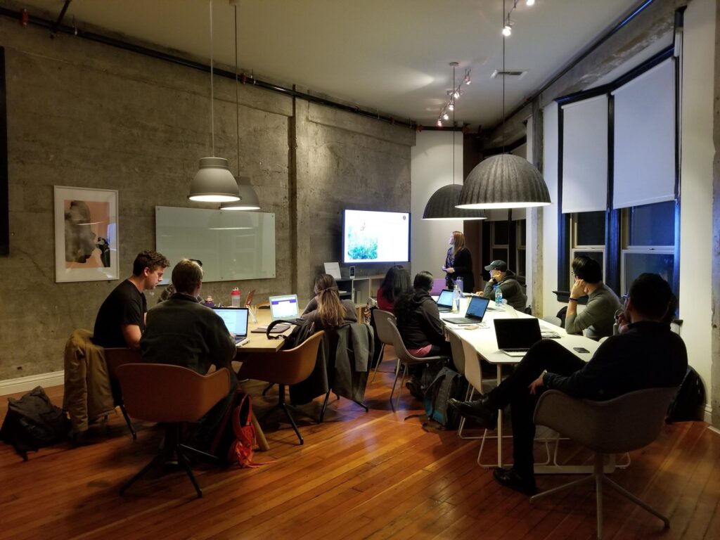 A diverse group of individuals engaged in discussion while seated at tables in a modern office environment.