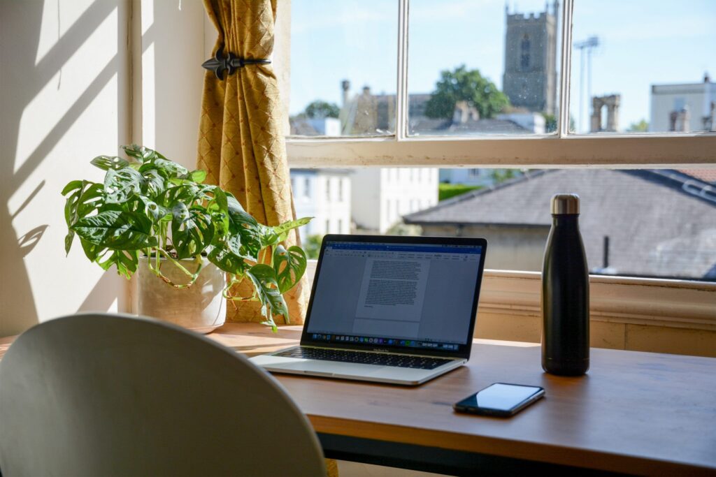 A laptop positioned on a desk beside a window, allowing natural light to illuminate the workspace.