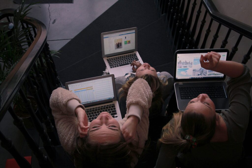 Three women seated on a stairway, each focused on their laptops, engaged in work or study.